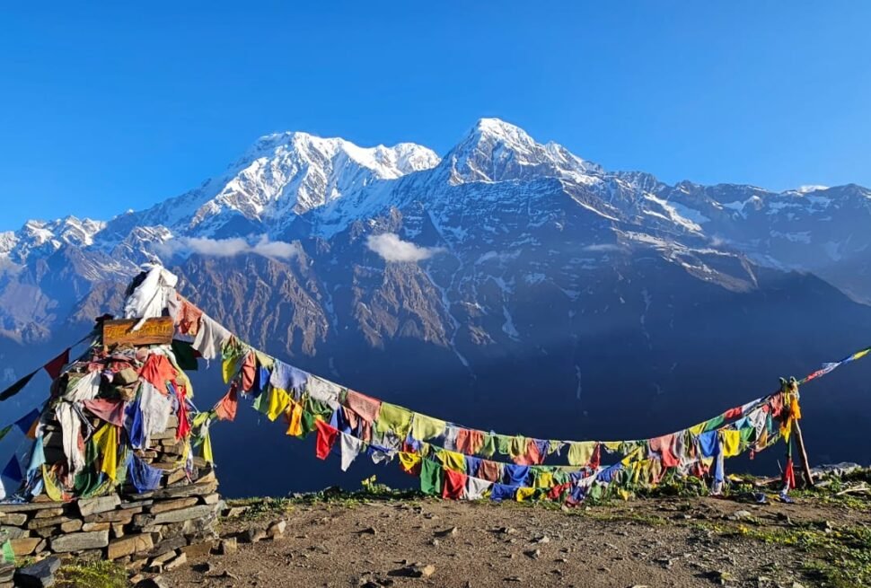 Prayer flags with snow-capped Himalayan mountains in the background under a clear blue sky.
