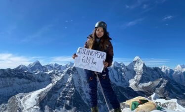 Climber Vanessa Fong standing on the summit of Island Peak (6,189m), holding a sign with breathtaking Himalayan peaks in the background.