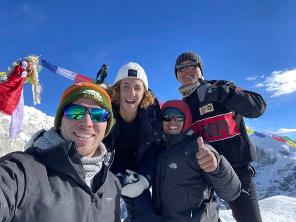 Happy climbers at Yala Peak summit with Tibetan prayer flags and snowy Himalayas in the background – Yala Peak Climbing Adventure.