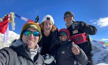 Happy climbers at Yala Peak summit with Tibetan prayer flags and snowy Himalayas in the background – Yala Peak Climbing Adventure.