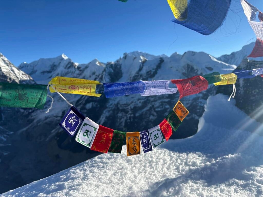 Tibetan prayer flags fluttering at Yala Peak summit with stunning snow-covered Himalayas in the background – Yala Peak Climbing, Langtang Valley Trek.