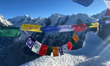 Tibetan prayer flags fluttering at Yala Peak summit with stunning snow-covered Himalayas in the background – Yala Peak Climbing, Langtang Valley Trek.
