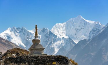 A majestic Buddhist stupa with snow-capped Himalayan peaks in the background, located in Kyanjin, Langtang Valley, under a bright blue sky.